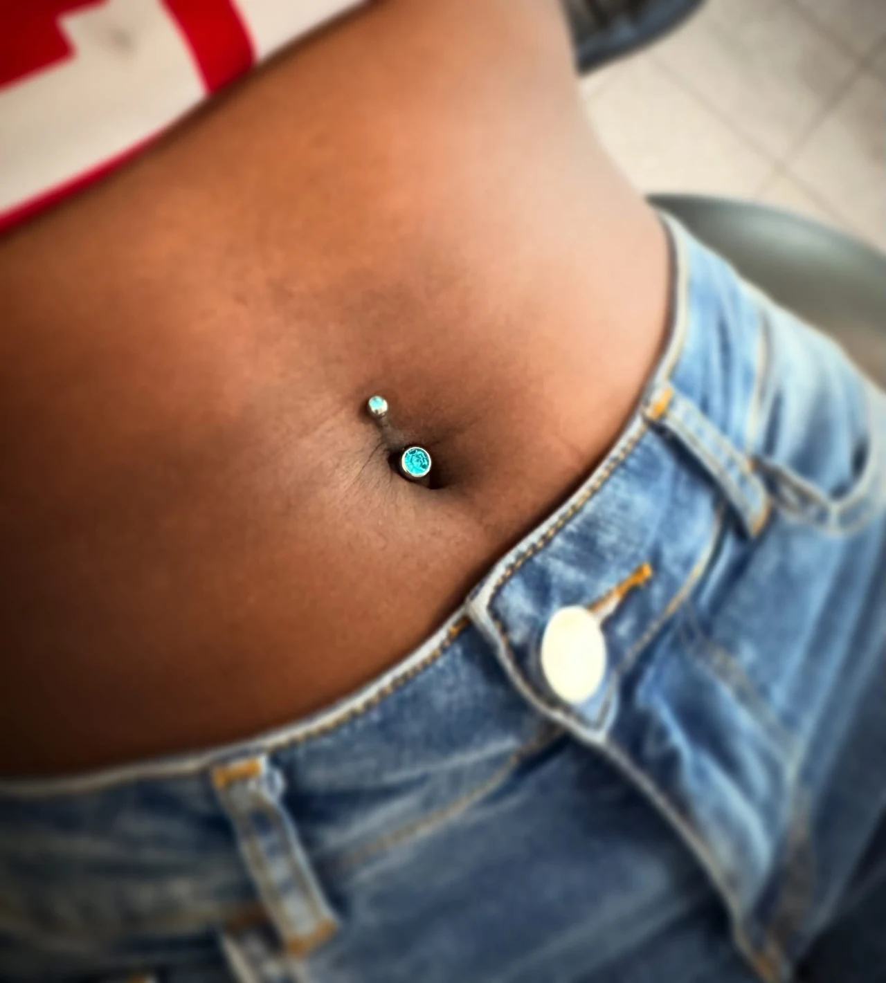 Nahaufnahme eines Bauchnabelpiercings mit türkisfarbenem Schmuck
